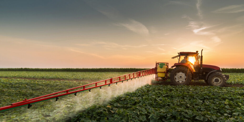 Agricultural tractor spraying pesticides on a green crop field